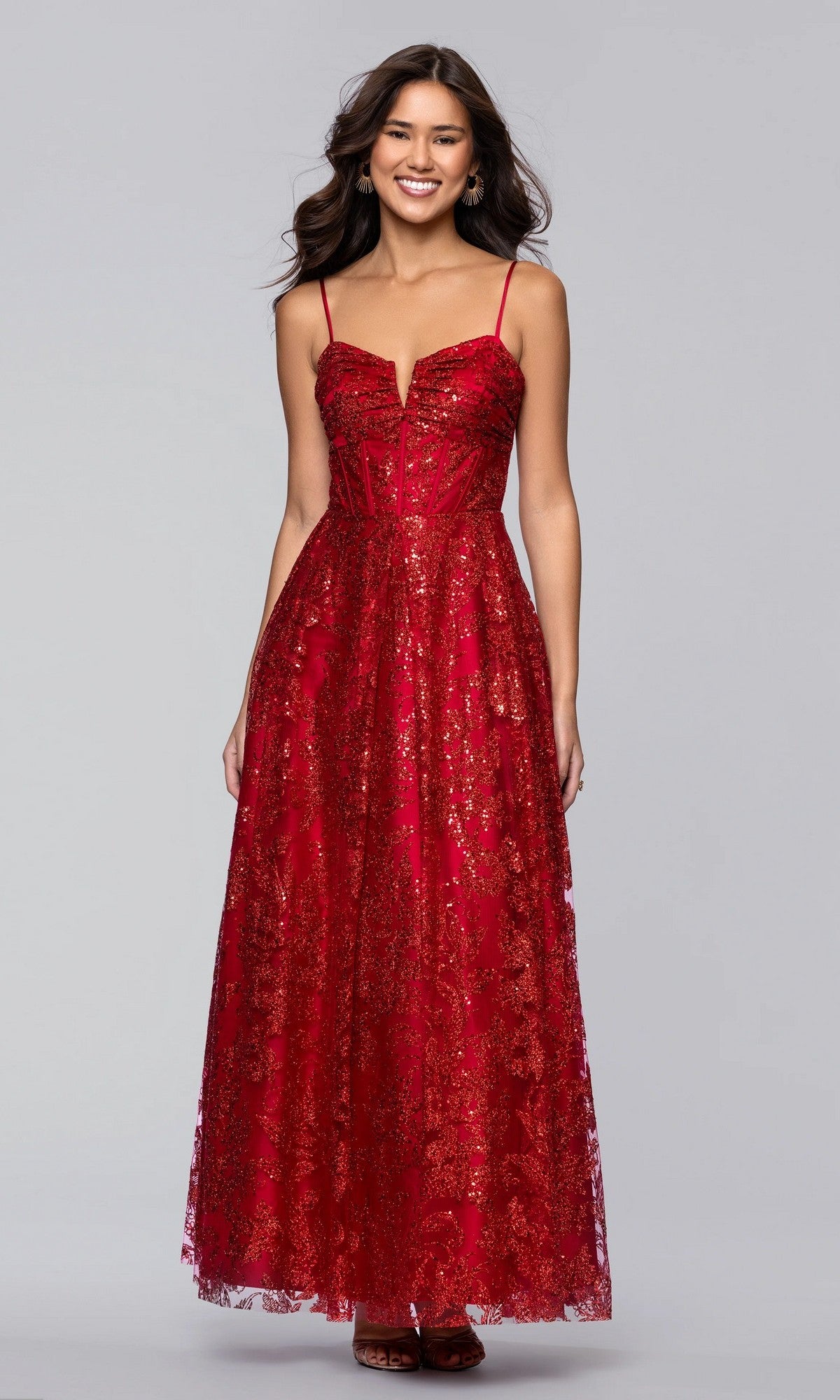 A woman smiles in the Blondie Nites 5409BN long red prom dress, featuring thin straps and a fitted corset bodice, posing elegantly against a plain light gray background.